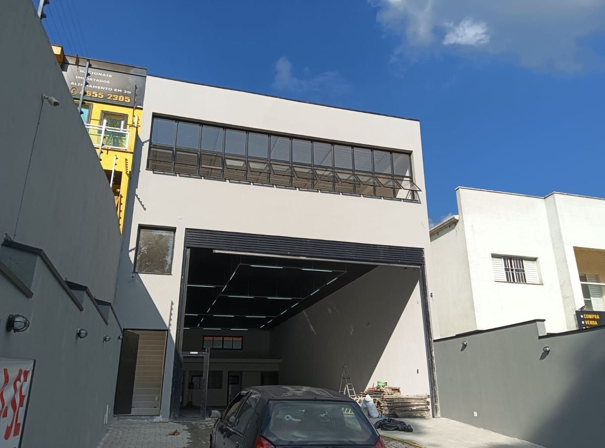 Galpão comercial de dois pavimentos com fachada fechada, esquadria contínua no andar de cima e portão amplo aberto para o salão.