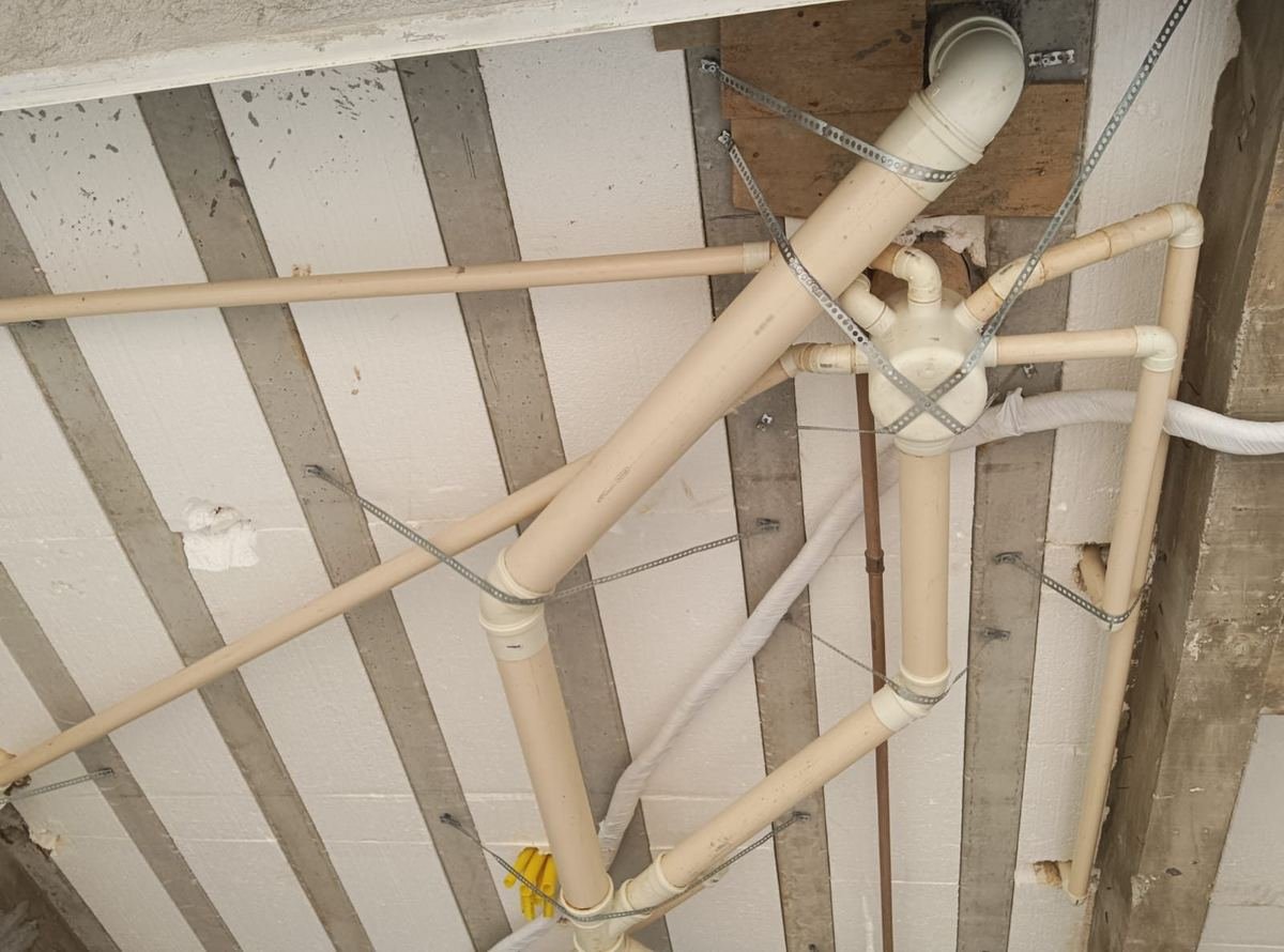 Tubulação de esgoto instalada sob laje pré-moldada, fixada por abraçadeiras metálicas em espaçamento regular, executada pela J&C Elétrica.