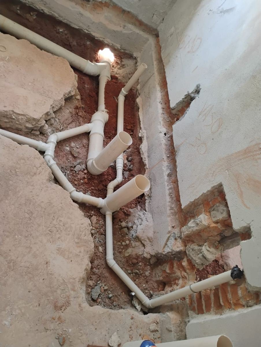 Parede aberta em obra com rede de esgoto em PVC montada dentro do rasgo, conexões e pontas aguardando a ligação das louças, executada pela J&C Elétrica.