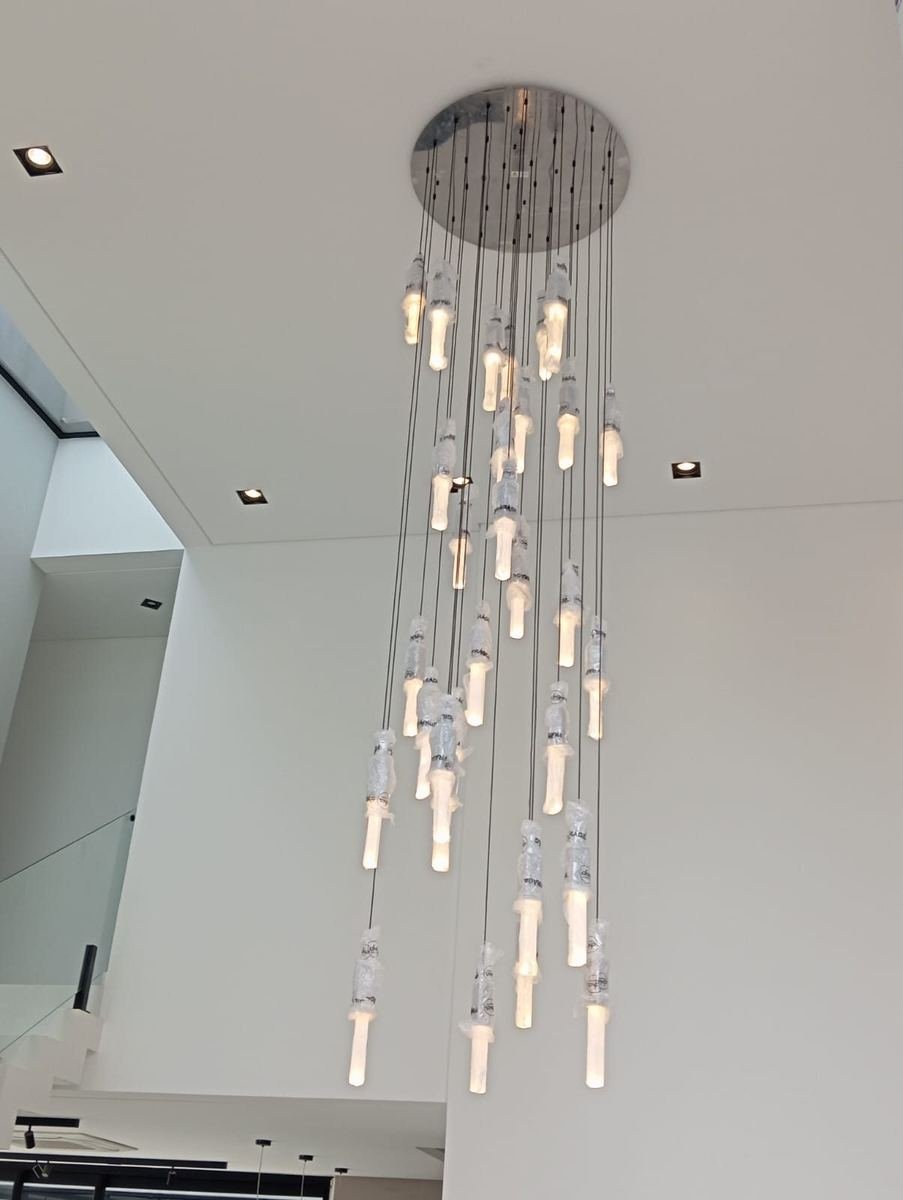 Lustre de dezenas de pendentes suspensos em pé-direito alto, acesos e ainda envoltos no plástico de proteção, instalados pela J&C Elétrica.