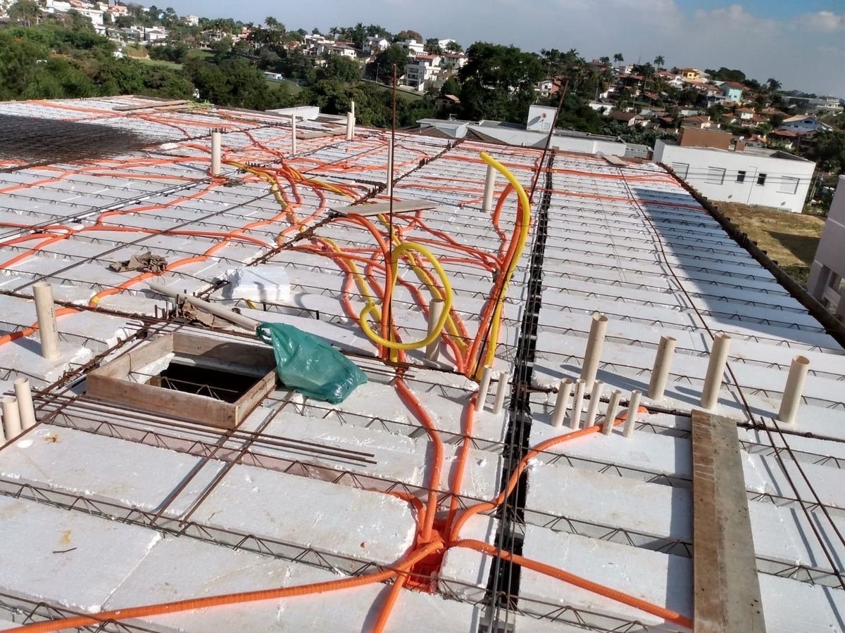 Laje de obra ainda armada, com eletrodutos corrugados laranja e amarelos amarrados à ferragem e caixas de passagem posicionadas, instalados pela J&C Elétrica.