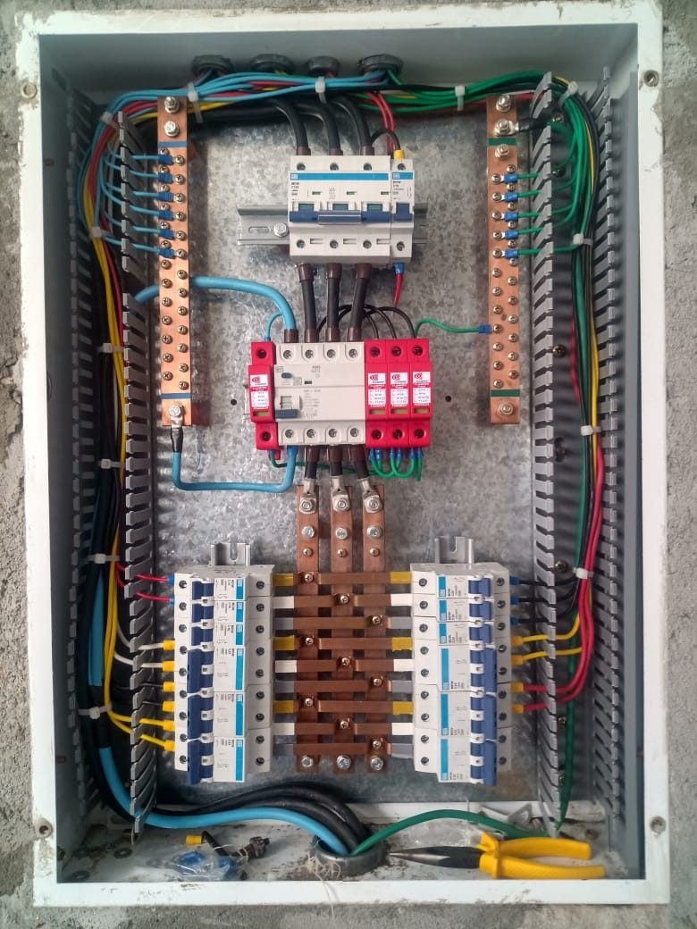 Quadro de distribuição aberto com disjuntor geral no topo, dispositivo DR e três protetores contra surto vermelhos logo abaixo, barramentos de neutro e terra nas laterais, montado pela J&C Elétrica.
